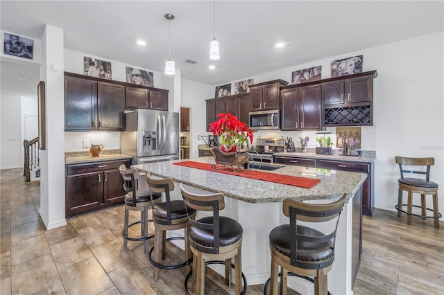 kitchen featuring light stone countertops, pendant lighting, a kitchen bar, a center island with sink, and appliances with stainless steel finishes