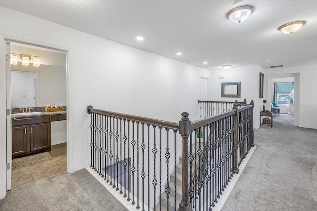 corridor with a textured ceiling, light colored carpet, and sink