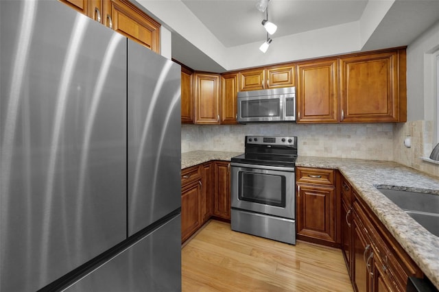 kitchen featuring sink, backsplash, light stone counters, stainless steel appliances, and light hardwood / wood-style flooring