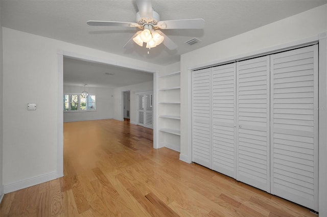 hallway with built in features, a textured ceiling, and light hardwood / wood-style floors