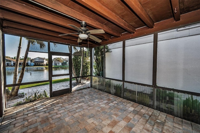 unfurnished sunroom featuring a water view, ceiling fan, beamed ceiling, and a wealth of natural light