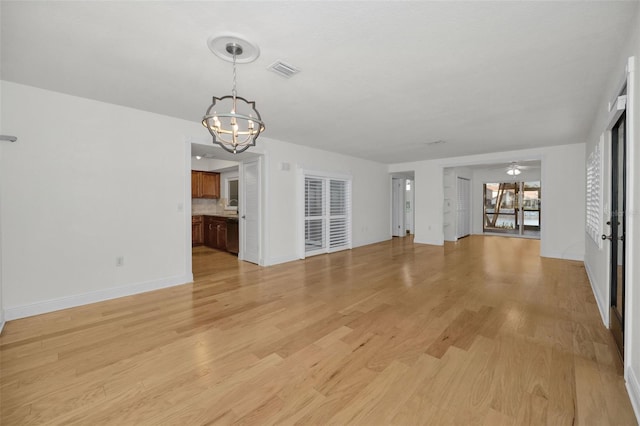 unfurnished living room with ceiling fan with notable chandelier and light hardwood / wood-style flooring