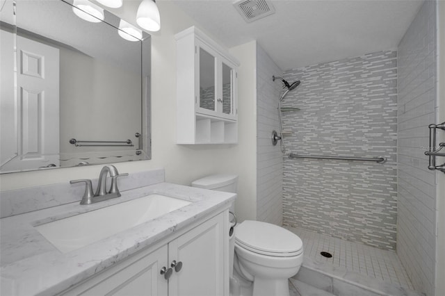 bathroom with vanity, tiled shower, a textured ceiling, and toilet