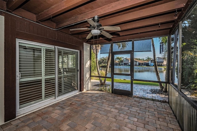 unfurnished sunroom featuring beamed ceiling, ceiling fan, and a water view