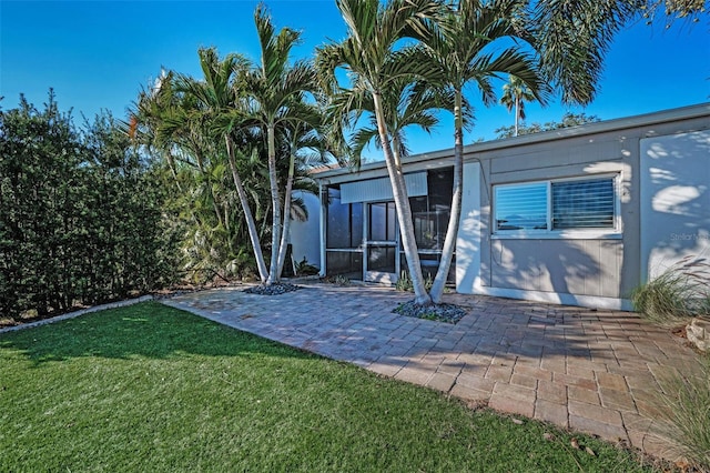 rear view of property featuring a patio, a sunroom, and a lawn