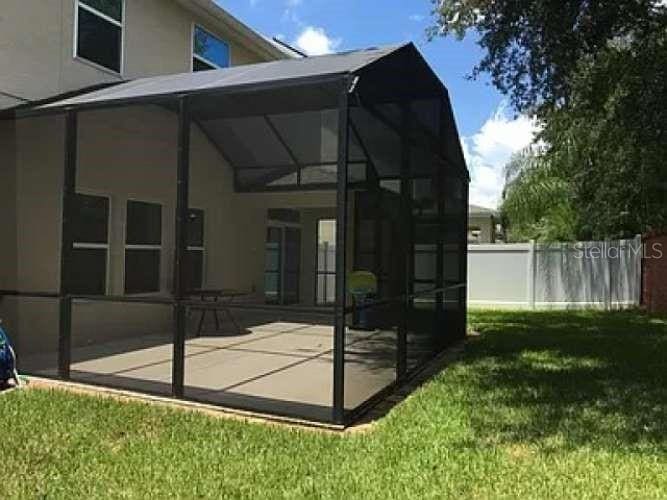 rear view of house featuring a lawn, glass enclosure, and a patio