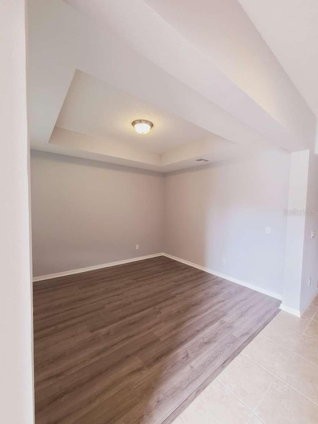 unfurnished room with a tray ceiling, wood finished floors, and baseboards