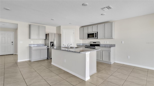 kitchen with sink, gray cabinets, a kitchen island with sink, light tile patterned floors, and appliances with stainless steel finishes