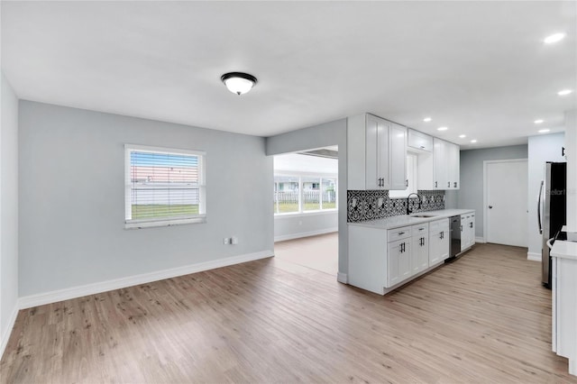 kitchen featuring white cabinets, sink, stainless steel dishwasher, decorative backsplash, and light hardwood / wood-style floors