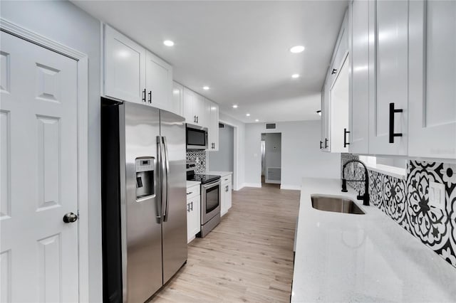 kitchen featuring white cabinetry, sink, light stone counters, decorative backsplash, and appliances with stainless steel finishes