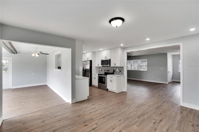 kitchen with white cabinets, ceiling fan, appliances with stainless steel finishes, tasteful backsplash, and light hardwood / wood-style floors