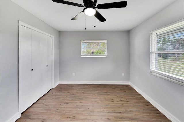 unfurnished bedroom featuring wood finished floors, a closet, baseboards, and ceiling fan