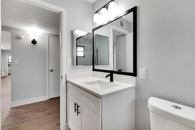 bathroom with wood finished floors, vanity, baseboards, toilet, and visible vents