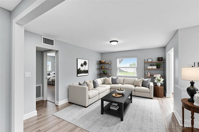 living room featuring light wood-type flooring, visible vents, and baseboards