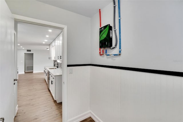 corridor featuring recessed lighting, light wood-style flooring, a wainscoted wall, and a sink