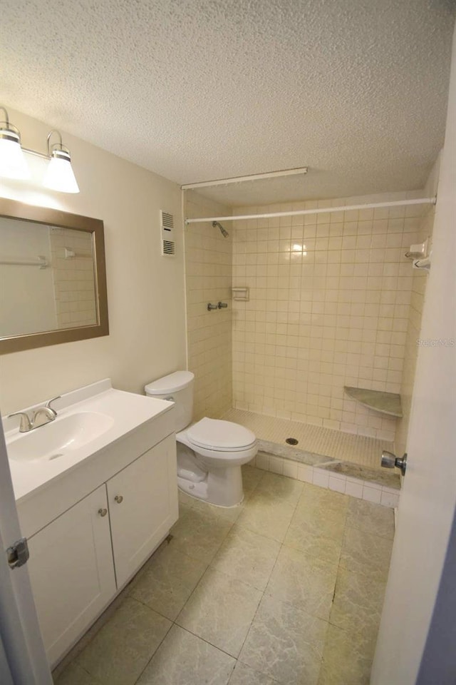 bathroom featuring tiled shower, vanity, a textured ceiling, and toilet