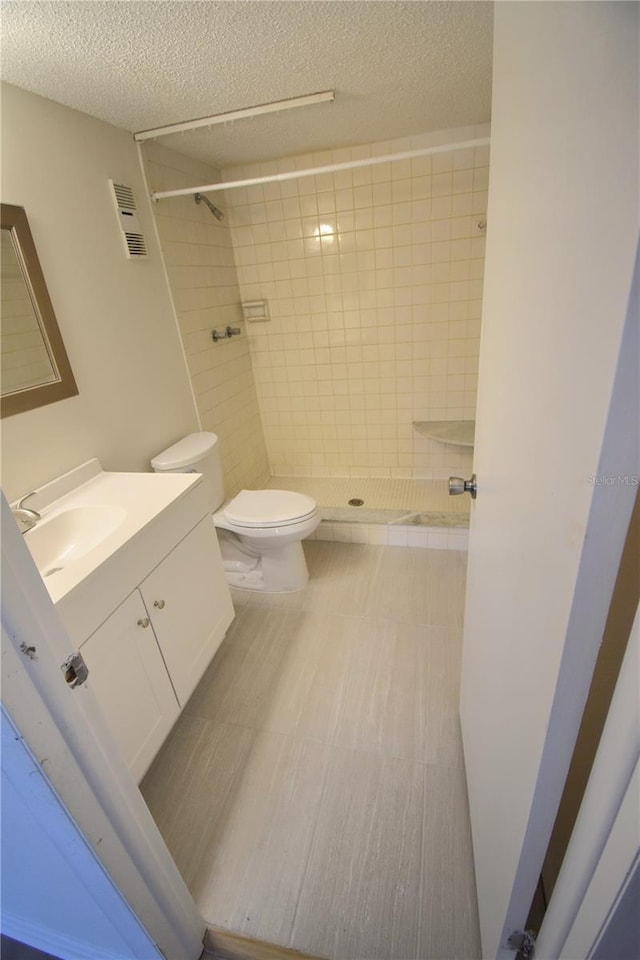 bathroom featuring tiled shower, vanity, a textured ceiling, and toilet