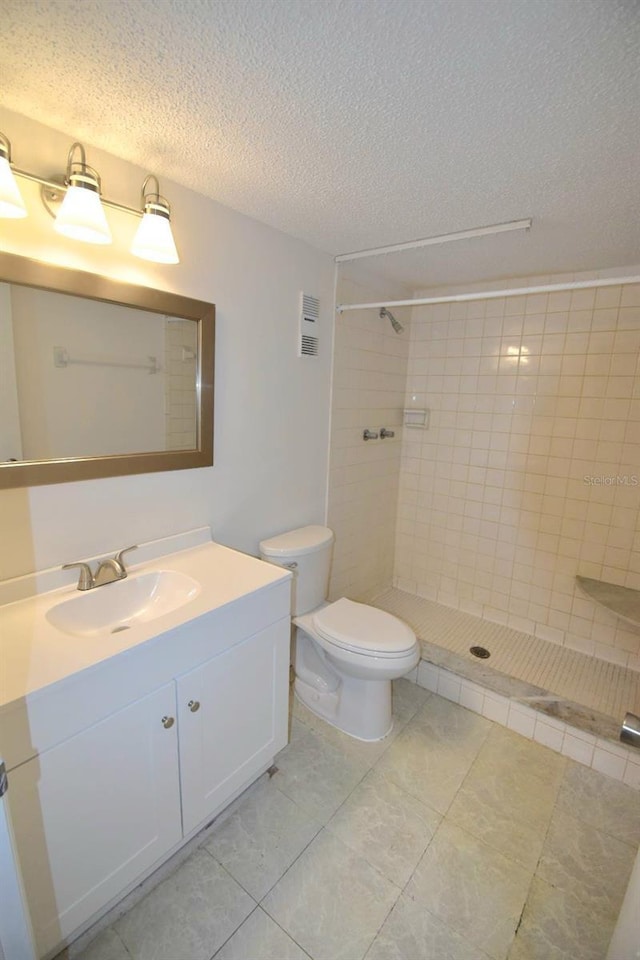 bathroom with tiled shower, a textured ceiling, vanity, and toilet