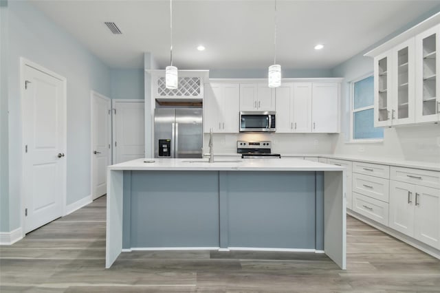 kitchen featuring white cabinets, sink, an island with sink, appliances with stainless steel finishes, and decorative light fixtures