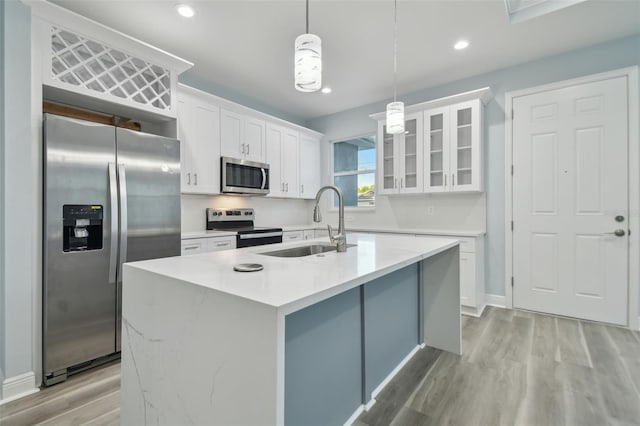 kitchen with appliances with stainless steel finishes, sink, white cabinets, hanging light fixtures, and an island with sink