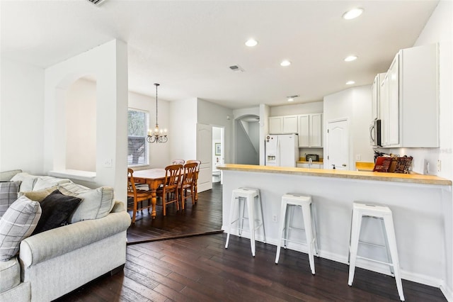 kitchen featuring kitchen peninsula, a breakfast bar, white fridge with ice dispenser, and white cabinets