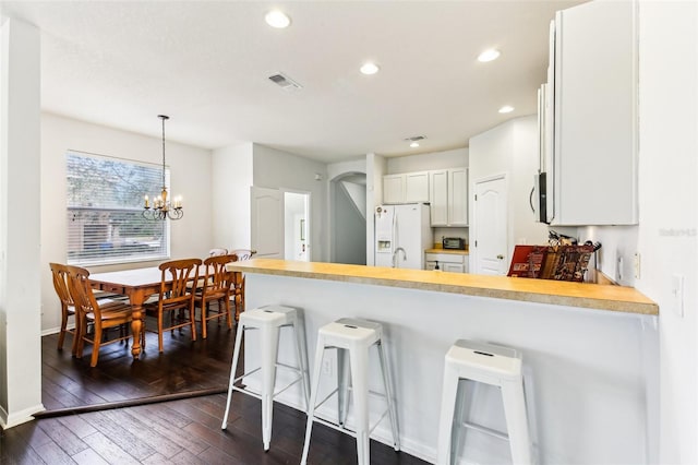 kitchen with hanging light fixtures, dark hardwood / wood-style flooring, white refrigerator with ice dispenser, a kitchen bar, and white cabinets