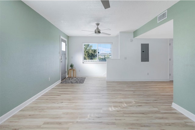 empty room with electric panel, ceiling fan, a textured ceiling, and light wood-type flooring