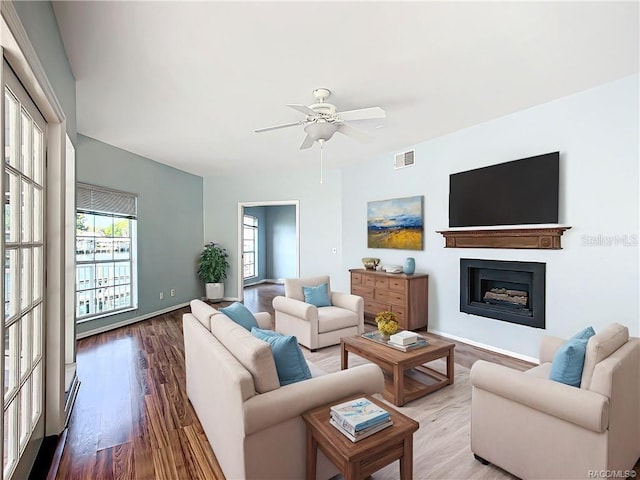 living area featuring baseboards, visible vents, a ceiling fan, wood finished floors, and a fireplace