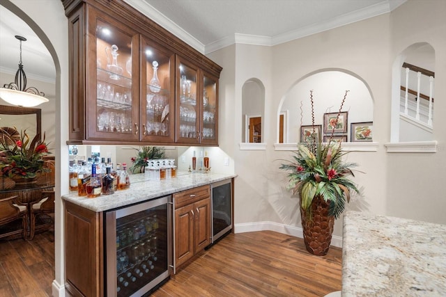 bar with light stone counters, hanging light fixtures, crown molding, and wine cooler