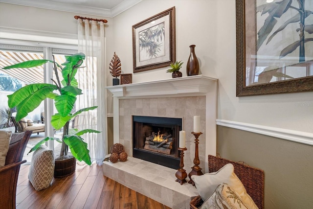 living area featuring a tile fireplace, crown molding, and hardwood / wood-style flooring