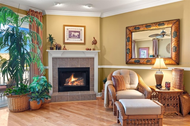 living area with wood-type flooring, ornamental molding, and a fireplace