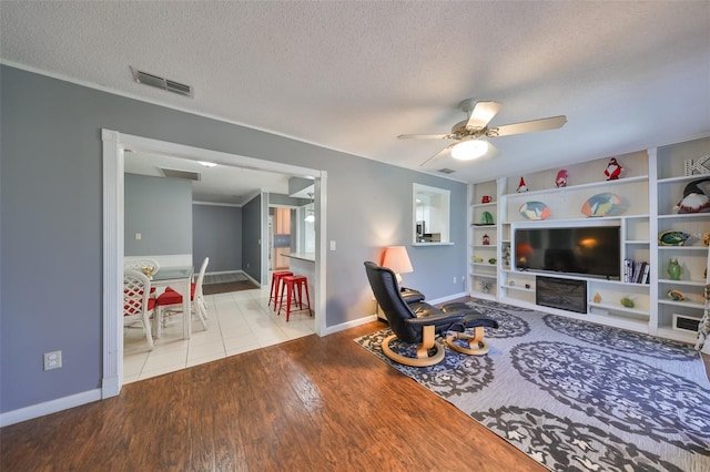 living room featuring ceiling fan, light hardwood / wood-style floors, a textured ceiling, and built in shelves