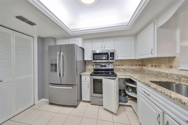 kitchen featuring decorative backsplash, light tile patterned floors, a tray ceiling, white cabinetry, and stainless steel appliances