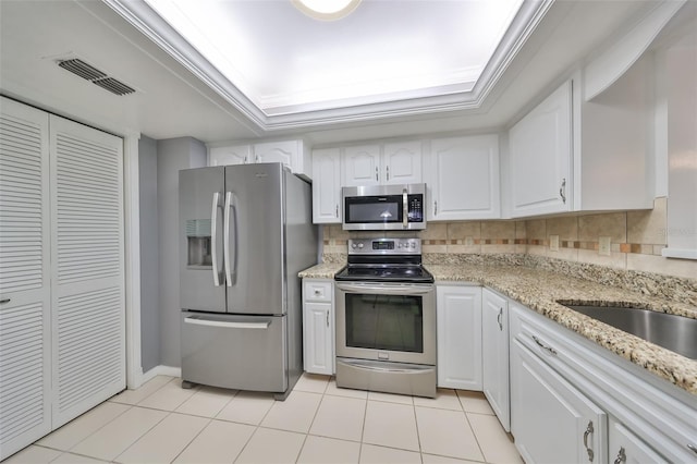 kitchen featuring light tile patterned floors, a raised ceiling, backsplash, white cabinets, and appliances with stainless steel finishes