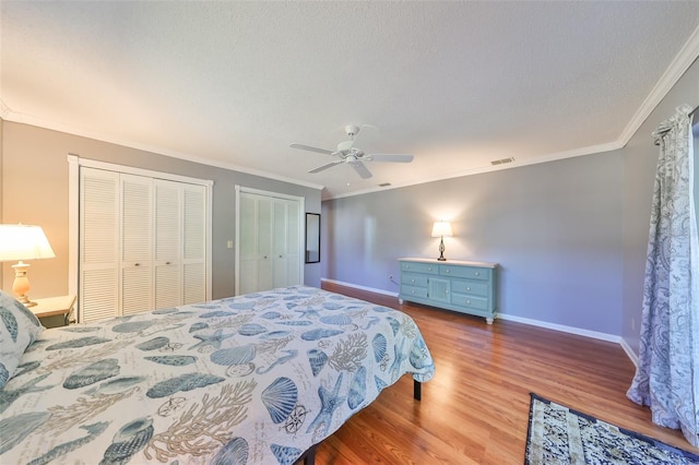 bedroom featuring multiple closets, ceiling fan, light hardwood / wood-style flooring, a textured ceiling, and ornamental molding