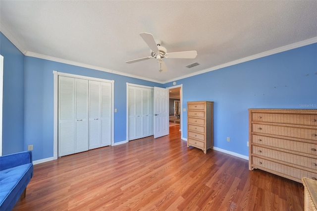 unfurnished bedroom featuring multiple closets, ceiling fan, wood-type flooring, and ornamental molding