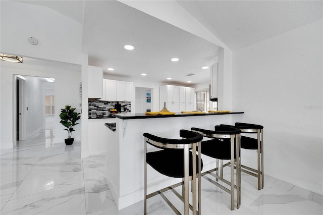 kitchen with white cabinetry, lofted ceiling, a kitchen breakfast bar, and kitchen peninsula