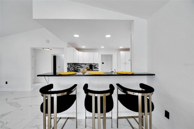 kitchen with lofted ceiling, white cabinetry, a kitchen breakfast bar, kitchen peninsula, and decorative backsplash