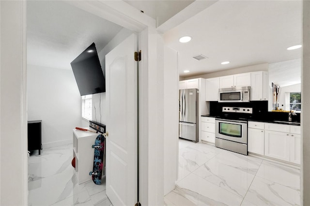 kitchen with tasteful backsplash, a healthy amount of sunlight, appliances with stainless steel finishes, and white cabinets