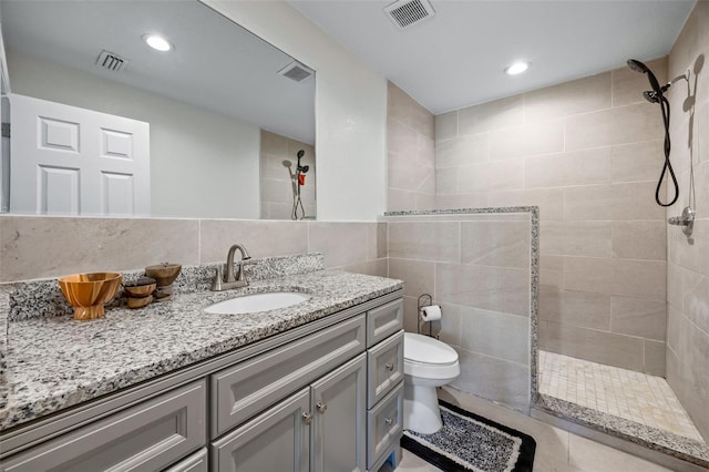 bathroom with a tile shower, vanity, tile walls, and toilet