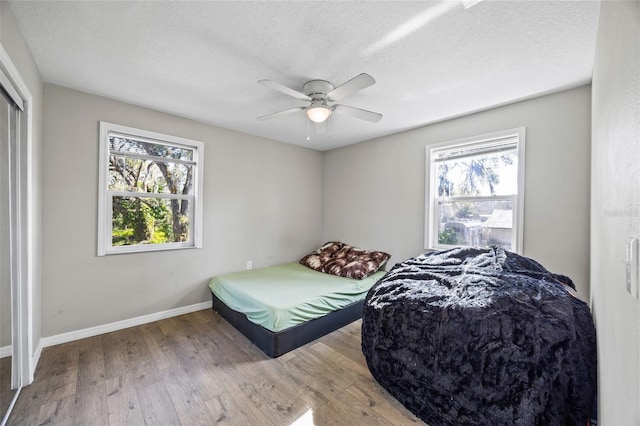 bedroom featuring ceiling fan, light hardwood / wood-style floors, a textured ceiling, and multiple windows