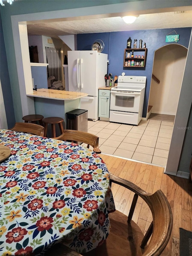 kitchen with a breakfast bar, white appliances, kitchen peninsula, and light tile patterned floors