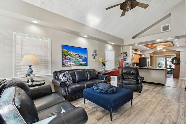 living room with light wood-type flooring, a textured ceiling, and vaulted ceiling