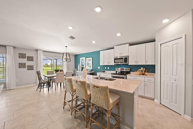 kitchen with white cabinetry, sink, hanging light fixtures, stainless steel appliances, and a center island with sink