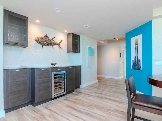 bar with dark brown cabinetry, light hardwood / wood-style floors, wine cooler, and light stone counters