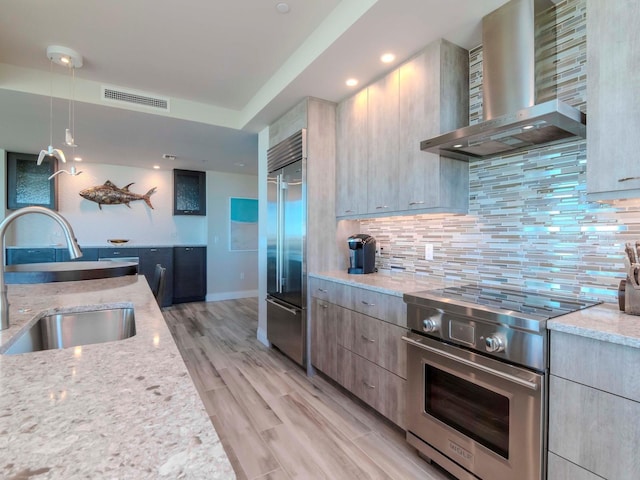 kitchen featuring wall chimney exhaust hood, high quality appliances, light stone countertops, and sink