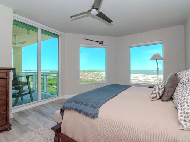 bedroom with access to exterior, light hardwood / wood-style floors, ceiling fan, and a water view