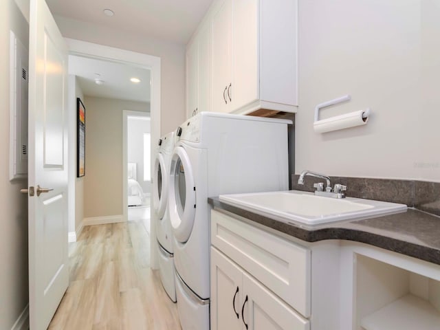 clothes washing area featuring light hardwood / wood-style flooring, cabinets, sink, and washing machine and clothes dryer