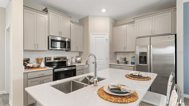 kitchen featuring sink, stainless steel appliances, tasteful backsplash, hardwood / wood-style floors, and a center island with sink