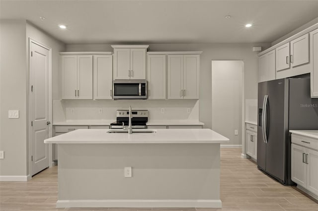 kitchen with stainless steel appliances, white cabinetry, a center island with sink, and light hardwood / wood-style floors